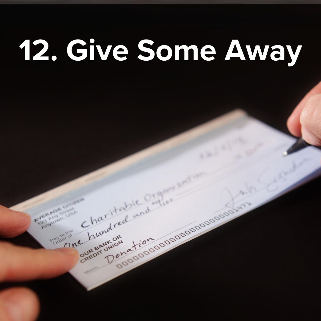 Black table background. Someone is filling out a check made to a Charitable Organization for a Donation. The white text title at top says: '12. Give Some Away'