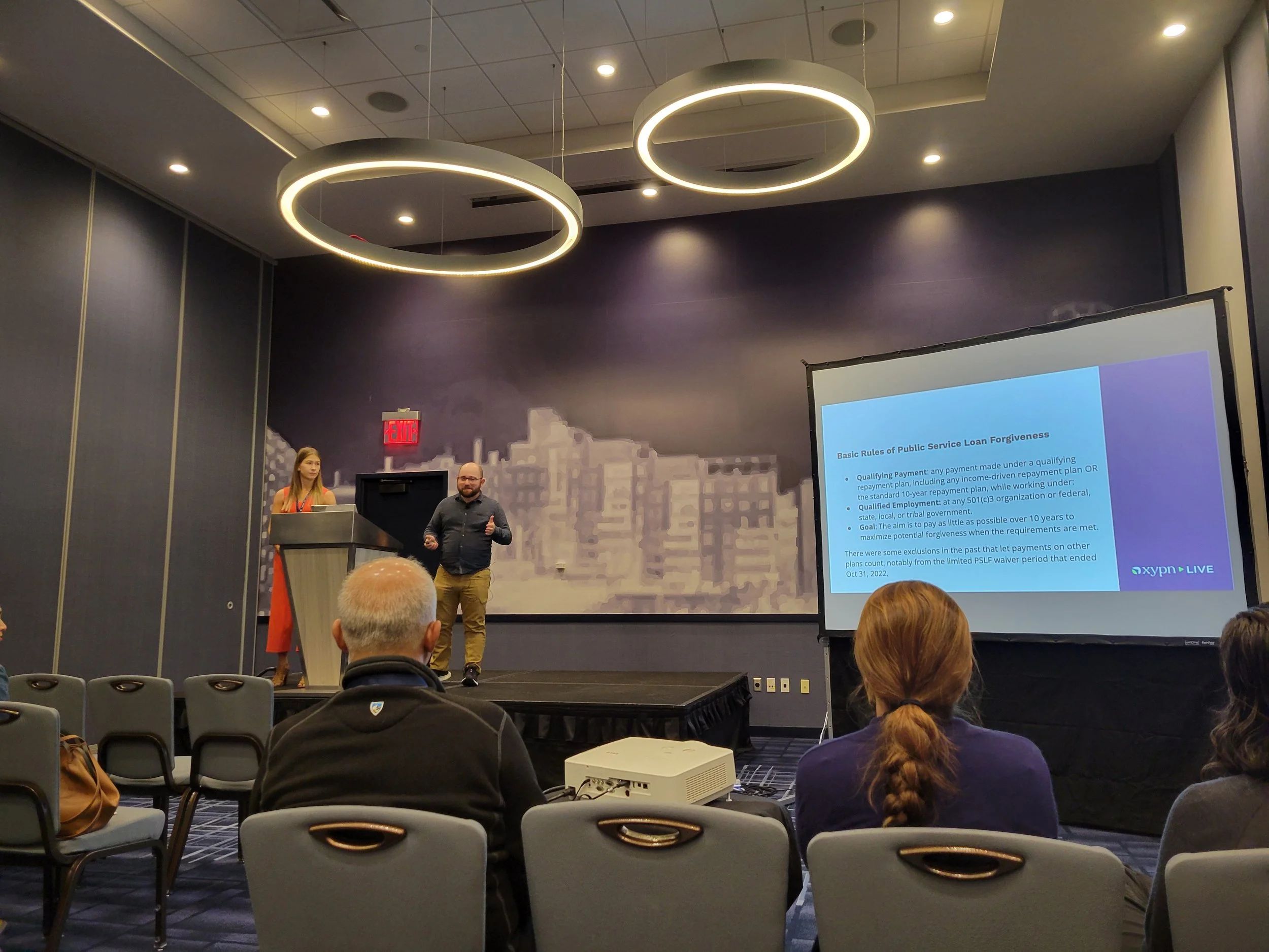 Photo of Autumn Knutson and Ethan Miller presenting to a crowd in a large hotel conference room.