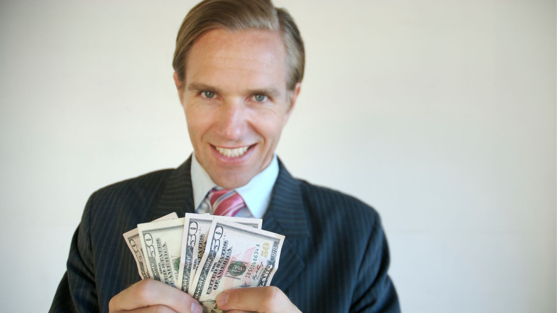 Man wearing a suit and red power tie smiling and holding four $50 bills.