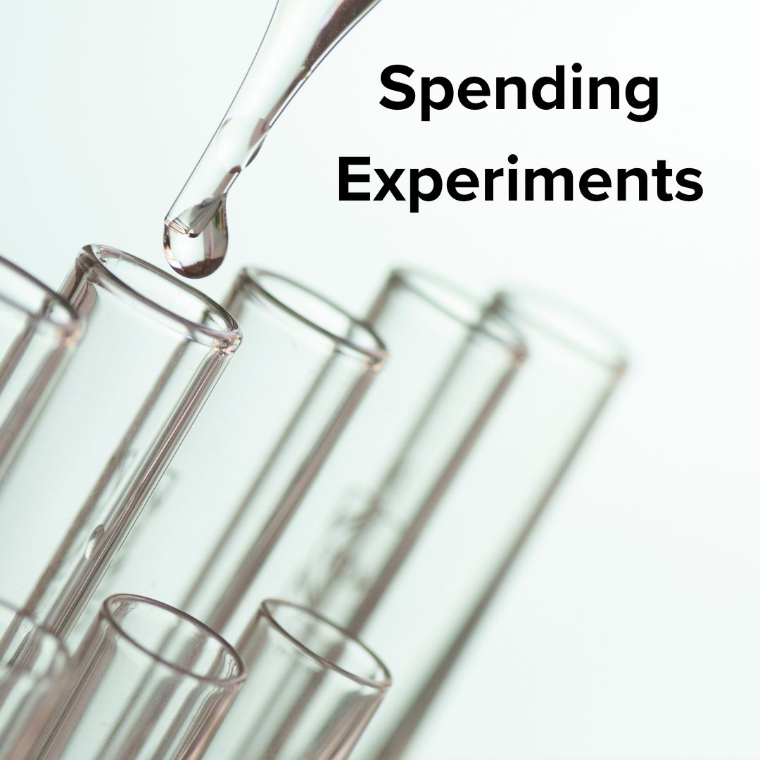 Title 'Spending Experiments' in black font. A dropper is dropping a bead of liquid into one of many test tubes.